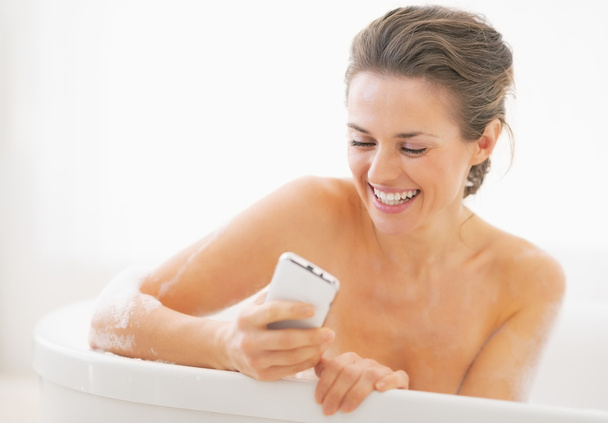 Smiling young woman in bathtub writing sms - Fotoğraf, Görsel
