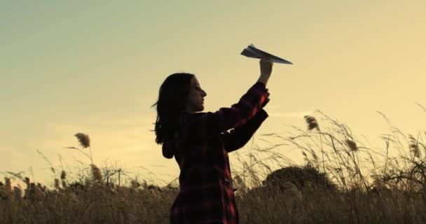 Νεαρή γυναίκα παίζει με χάρτινο αεροπλάνο στον τομέα του σιταριού - Πλάνα, βίντεο