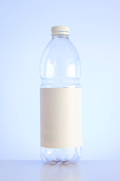 Чистая пустая пластиковая бутылка с красной крышкой и белой пустой этикеткой, изолированной на светло-синем фоне вертикальным снимком. - Фото, изображение