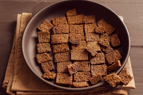 There is a picture of food on a wooden background. In a cast-iron pan is fried and dry black bread. The bread is not whole, it is divided into small pieces that can be used as a way to have a quick snack - Foto, Imagem