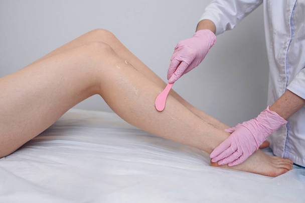 Laser epilation and cosmetology in beauty salon, spa concept. Preparation for the procedure of laser hair removal. Application of gel, disposable spatula. Beautiful smooth female legs - Photo, Image