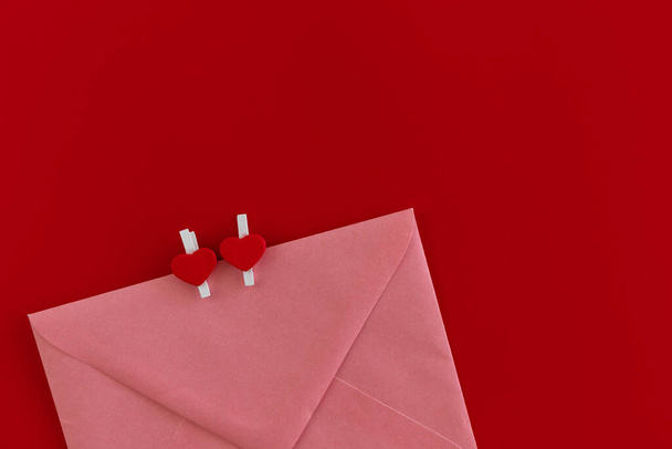 Widok z góry zdjęcie różowej koperty z dwóch szpilek w kształcie serca izolowane na czerwonym tle. Poczta wakacyjna. Koncepcja tła Walentynek. Świąteczna makieta. List miłosny. Romantyczny list miłosny - Zdjęcie, obraz