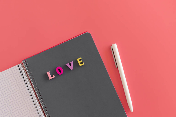 カラフルな文字の碑文の愛とピンクの背景に白いペンとグレーのシートでスパイラルノートを開きました。バレンタインデーのテキスト、愛とロマンスのコンセプト、トップビューのためにモックアップします。メッセージを書く - 写真・画像