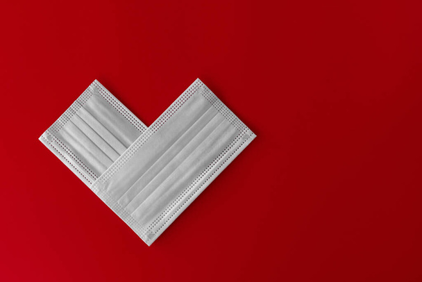 Duas máscaras médicas brancas de close-up empilhadas na forma de um coração em fundo vermelho com espaço para texto. Tema da bandeira do amor. Amoroso, emoções positivas. O conceito de celebração e amor. - Foto, Imagem