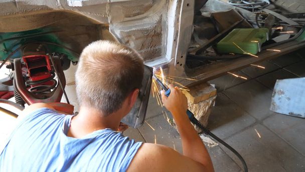 Onherkenbaar reparateur dragen beschermende masker lassen een aantal detail van de auto. Mechanisch werken in garage of werkplaats. Een man die auto 's repareert. Auto reparatie en onderhoud concept. Dolly schot. - Foto, afbeelding