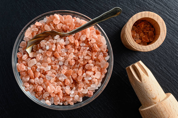 Skleněná miska himálajské soli s malou lžičkou a dřevěnou solnou mlýnkou na černém pozadí  - Fotografie, Obrázek