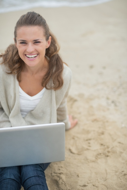 Happy woman sitting with laptop on beach - Foto, afbeelding