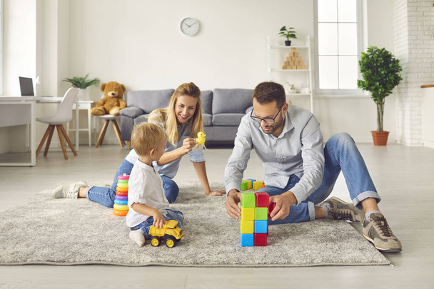 Mom and dad play with their son at home with a variety of toys and colored cubes sitting in a room. - Fotoğraf, Görsel