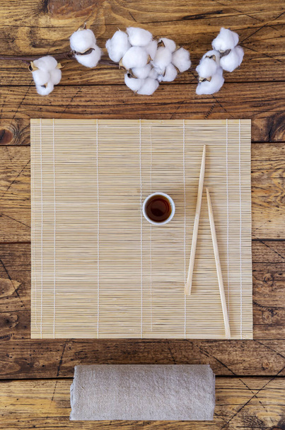 Oriental-style background with a mat with chopsticks and soy sauce and sprig of cotton - Fotografie, Obrázek