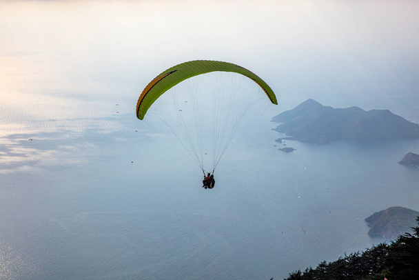 Gökyüzünde paraşütle atlıyor. Paraglider gün batımında dağlarla birlikte denizin üzerinde uçuyor. Oludeniz, Babadag, Mugla, Türkiye 'deki Paraşütçü ve Mavi Göl manzarası. - Fotoğraf, Görsel