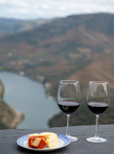 Tasting of Portuguese red dry wine, produced in Douro Valley with goat and sheep cheese and Douro river and terraced vineyards on background in autumn, North of Portugal - Photo, Image