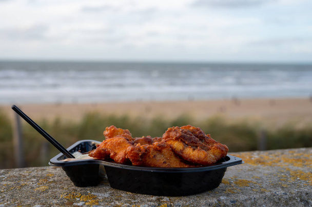 Ολλανδικά θαλασσινά δρόμο, τηγανητά ψάρια μπακαλιάρου φιλέτο με σάλτσα σκόρδου που ονομάζεται στην Ολλανδία kibbeling και τη Βόρεια θάλασσα παραλία στο παρασκήνιο το χειμώνα - Φωτογραφία, εικόνα
