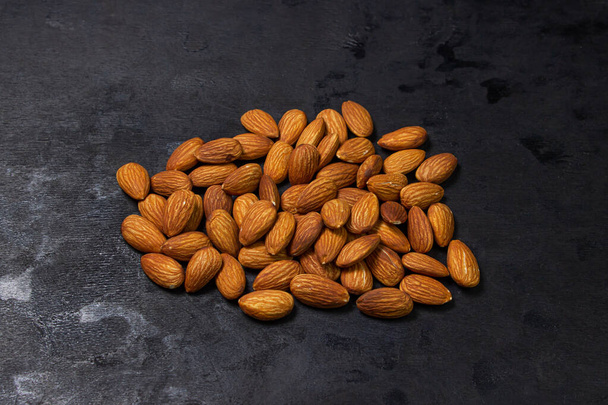 Almonds on a black background. Isolated almonds. Small pile of roasted almonds - Photo, Image