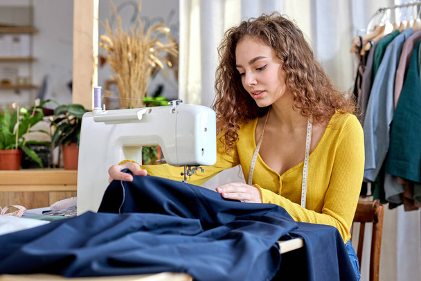 work with fabric. beautiful caucasian dressmaker tailoring while sitting at sewing machine looking seriously - Valokuva, kuva