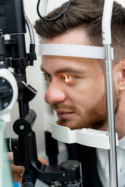 Handsome man is getting an eye exam at ophthalmology clinic. Male is checking retina. Close-up - Foto, immagini