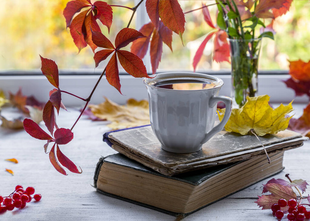 A cup of tea on a wooden windowsill with a bouquet of autumn leaves on a natural background.  - Photo, Image