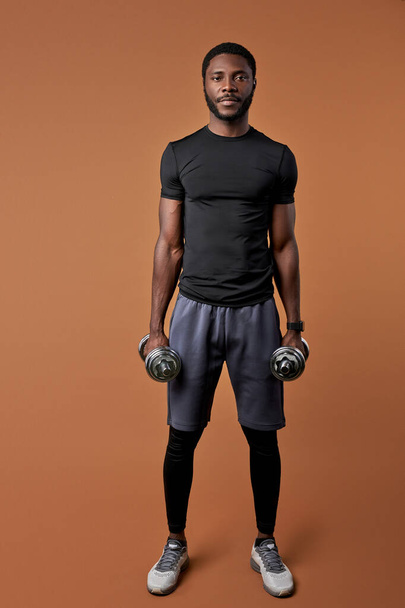 full-length portrait of sportsman pumping arm muscles using dumbbells - Foto, afbeelding