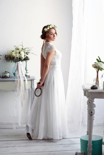 Bride in an elegant white dress near the window on the wedding day. Romantic morning with beautiful decor - Foto, afbeelding