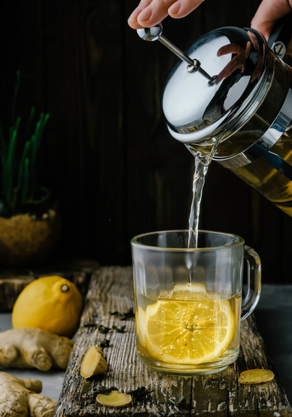 Gember thee met citroen wordt gegoten in een glas van een theepot, close-up, ingrediënten voor thee op een houten vintage tafel. Preventie en ondersteuning van immuniteit - Foto, afbeelding