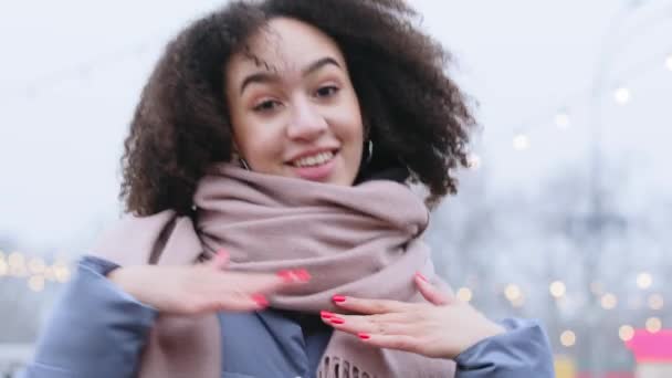 Portret van vrolijke vrouwelijke student tiener dame donker-gevild vrolijk meisje met stijlvolle krullend afro haar draagt modieuze sjaal staat alleen buiten in de winter dansen beweegt haar armen handen actief - Video