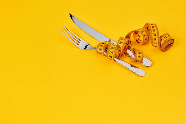 Couteau et fourchette avec ruban à mesurer sur fond jaune - Photo, image