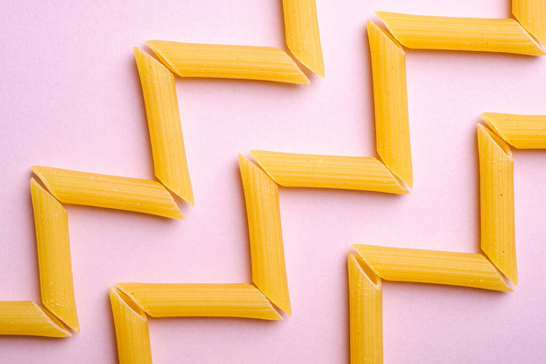 Italian pasta, raw penne tube macaroni zigzag pattern on pink background, top view, abstract food - Fotoğraf, Görsel