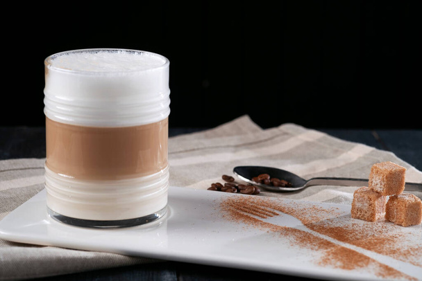 Üveg csésze kávé latte macchiato vagy cappuccino habbal sötét alapon szolgálja fel az asztalon - Fotó, kép