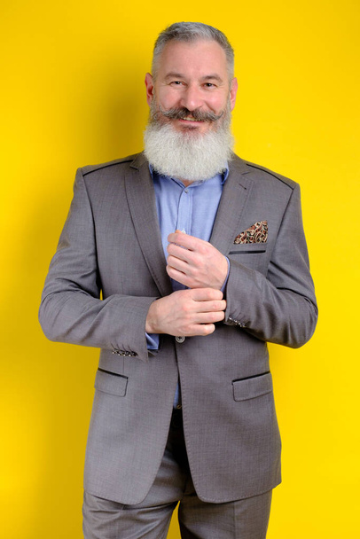 Студия портрет зрелый бородатый красивый мужчина в сером деловом костюме, глядя на камеру, трудовую профессию образ жизни, желтый фон. - Фото, изображение
