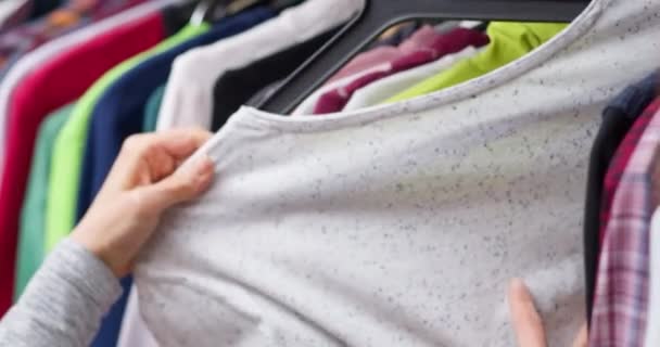 Een vrouw kiest kleren aan een hanger om te winkelen. Close-up van een hand kopen van kleding. - Video