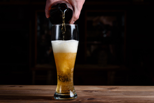  Vaso con cerveza en una mesa de madera. La cerveza se vierte en un vaso de una botella. - Foto, Imagen