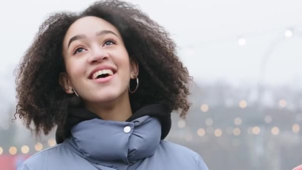 Portret van een afro-Amerikaanse vrouw met krullend haar staat buiten in de winter in warme buitenkleding ademt stoom uit haar mond maakt de winter koude wind lacht plezier in de stad in lage temperatuur klimaat - Video