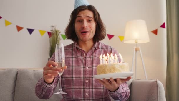 Screenshot of young man in party cap saying Happy Birthday and drinking champagne, greeting to camera with cake - Footage, Video