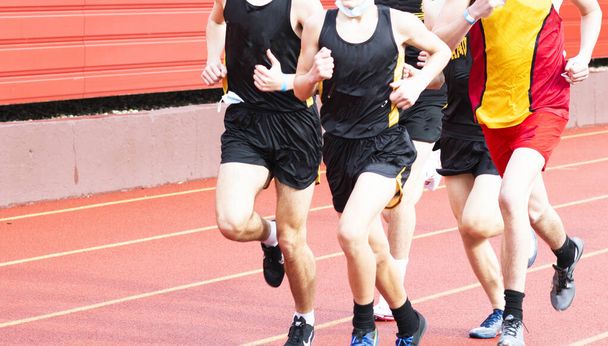 Atletas de atletismo de secundaria corriendo una carrera al aire libre durante la pandemia de coronavirus COVID-19 con mascarillas en la mano. - Foto, Imagen