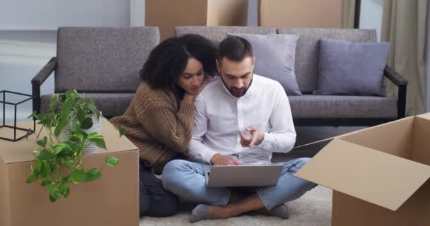 Smíšené závod pár mnohonárodnostní rodina africká americká žena a běloch muž sedí na podlaze nového domu obklopen boxy výběru zboží on-line nakupování on-line objednávání nákladní služby přesunout - Záběry, video