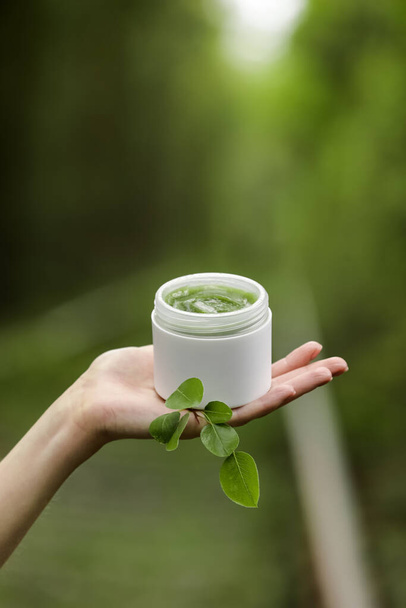 Young Female hands hold a jar of green natural cream for face or body. organic natural skincare products on green natural background. Packaging of lotion or cream. Beauty cosmetic skin care concept - Foto, immagini