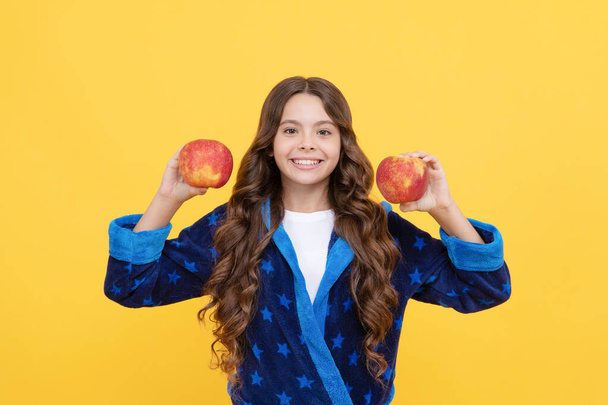 menina adolescente alegre com cabelo encaracolado em pijama confortável vai comer maçã saudável, vitamina. - Foto, Imagem