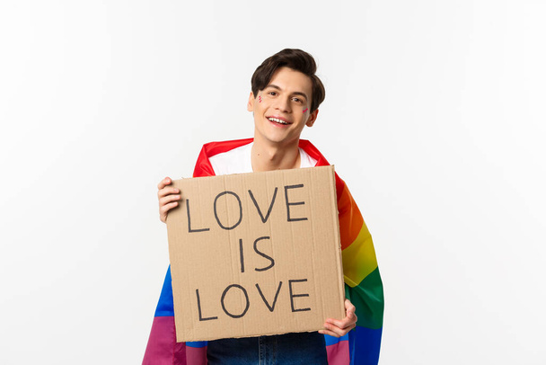 sorridente gay uomo attivista holding segno amore è amore per lgbt orgoglio parata indossare arcobaleno bandiera in piedi su bianco sfondo - Foto, immagini