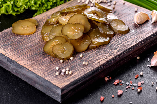Sabroso pepino picante salado en vinagre cortado con anillos en una tabla de cortar de madera sobre un fondo de hormigón oscuro - Foto, Imagen