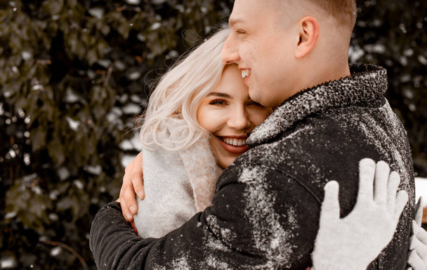 Ένα αξιαγάπητο ζευγάρι σε μια τρυφερή αγκαλιά. Ο τύπος φιλάει την κοπέλα του. Ημέρα του Αγίου Βαλεντίνου. Ο νεαρός αγκαλιάζει την κοπέλα του στο χειμερινό πάρκο.. - Φωτογραφία, εικόνα