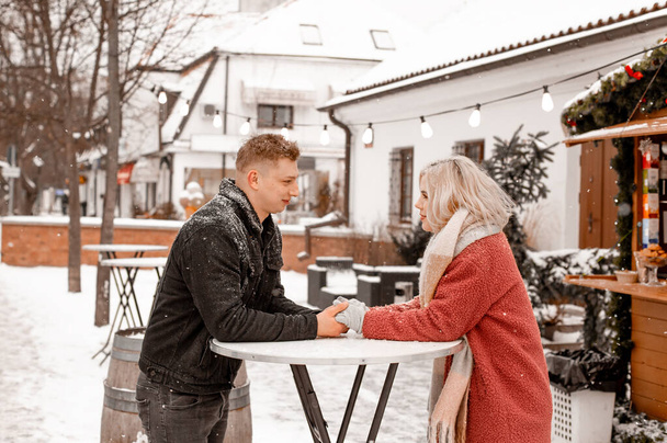 Happy young couple standing at table at open air Christmas market. Theme love holiday Valentines Day. Emotion romance of happiness and love. - Fotografie, Obrázek
