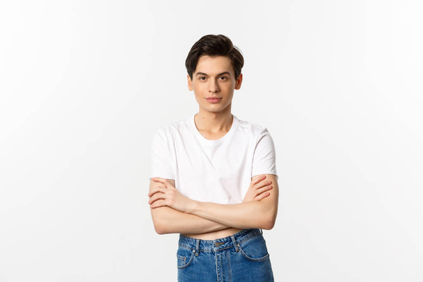 Image of sassy gay man in crop top smiling, looking confident, cross arms on chest and standing over white background - Foto, immagini