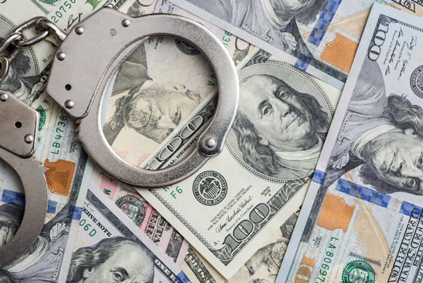 Handcuffs on money background. Dollar bills, money cash corruption, dirty money financial crime and metal police handcuffs. - Photo, Image