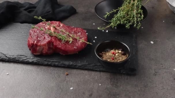 fresh raw beef steak decorated with spices and thyme on black stone plate zoom in - Footage, Video