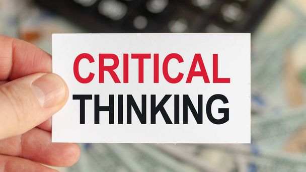 Słowa motywacyjne: CRITICAL THINKING. Człowiek trzyma kawałek papieru z tekstem: CRITICAL THINKING. Koncepcja biznesowa i finansowa - Zdjęcie, obraz