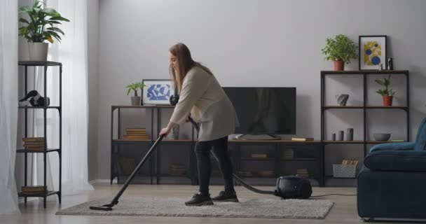 nuori nainen käyttää pölynimuria olohuoneessa, siivous kotiin viikonloppuna, kotiäiti tekee kotitöitä - Materiaali, video