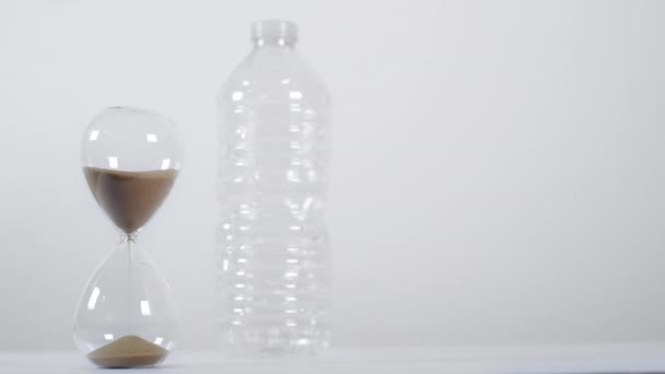 Plan large d'une minuterie à sable à côté d'une bouteille en plastique à usage unique sur fond blanc - Séquence, vidéo
