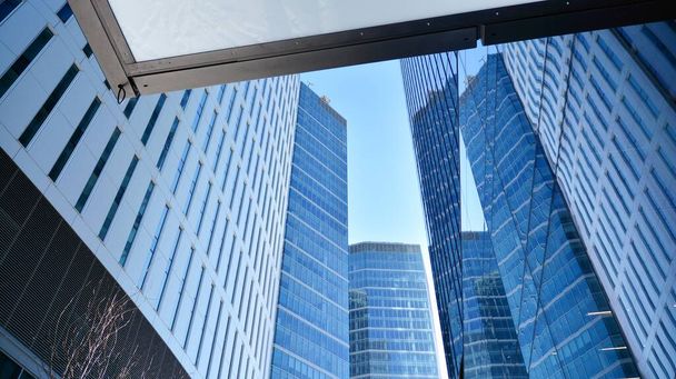 Γυάλινη πρόσοψη των κτιρίων με γαλάζιο ουρανό. Ουρανοξύστες στο επιχειρηματικό κέντρο της πόλης.. Ιστορικό των σύγχρονων γυάλινων κτιρίων.  - Φωτογραφία, εικόνα