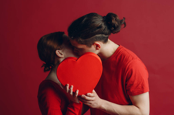 Man and woman young couple kissing and hiding behind heart-shaped box - Фото, изображение