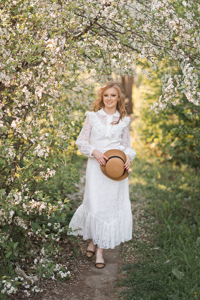 Portrait of a girl in a white lace dress with her hair flying in the wind and a straw hat in her hands. - Photo, Image