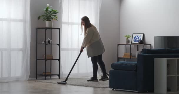 serviço de limpeza, trabalhador feminino está limpando tapete na sala de estar do apartamento moderno, usando aspirador de pó - Filmagem, Vídeo
